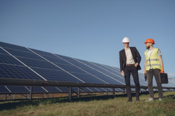 Businessman and engineer discussing solar energy solutions at a solar panel installation site, emphasizing modernization and compliance in energy distribution.